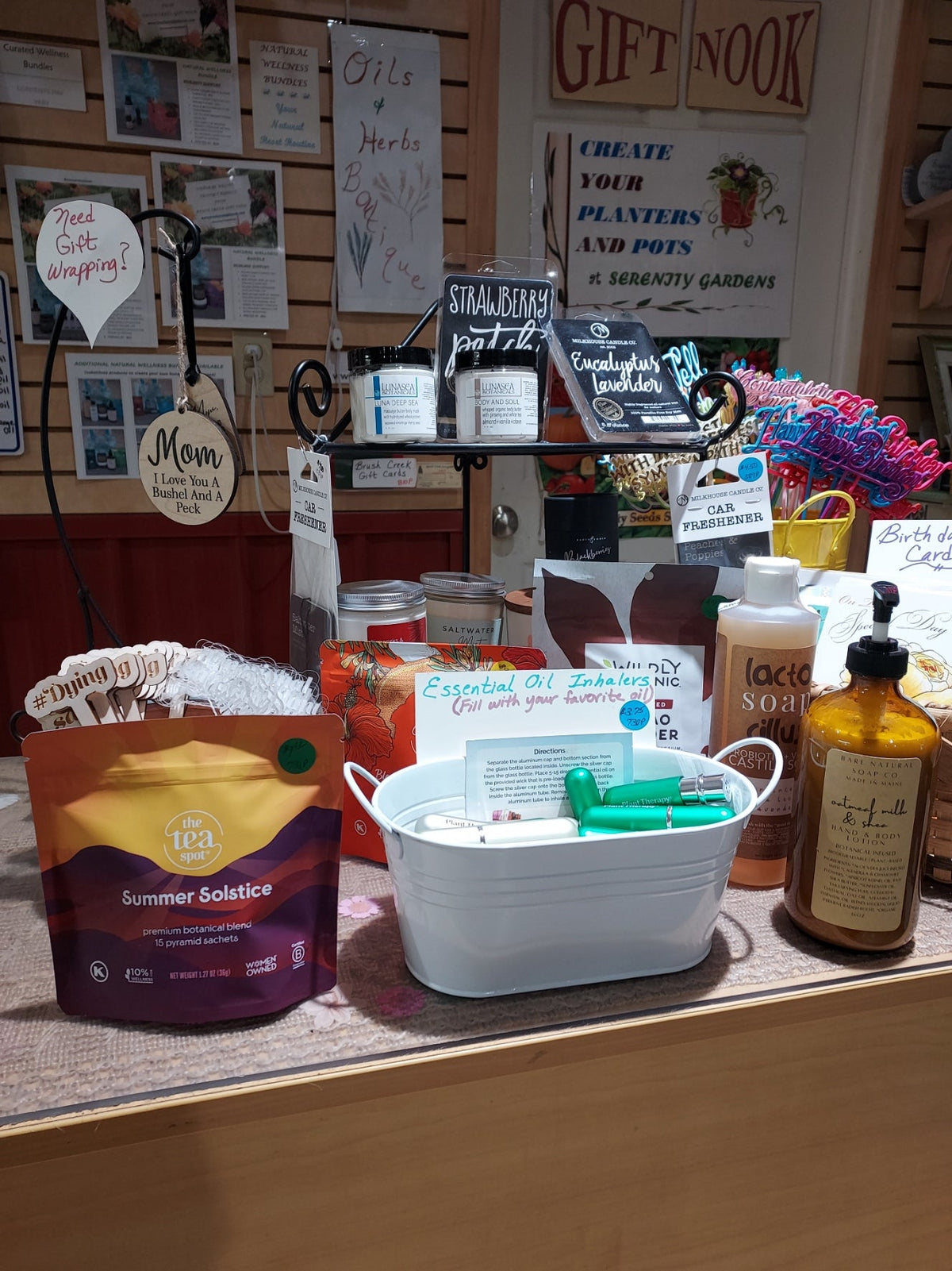 Collection of summer products displayed on the Brush Creek Evergreens Gift Nook sales counter, including teas, soaps, candles, body butters, gift cards, aromatherapy inhalers