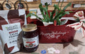 Holiday Comfort Bundle from Brush Creek featuring a Christmas cactus, fermented cacao powder, holiday berry jam, and decorative red Happy Holidays tin with seasonal greenery
