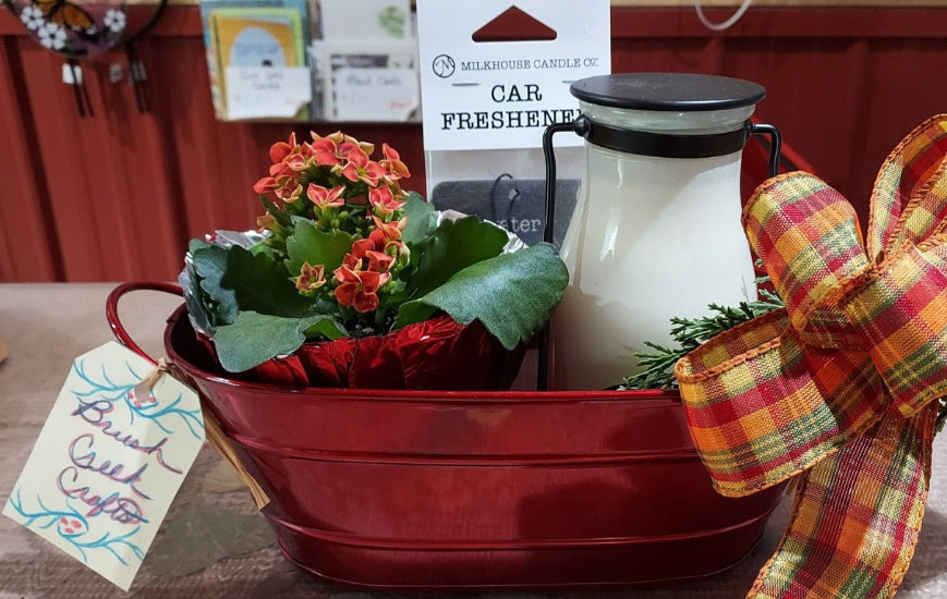 Brush Creek Bloom Bundle featuring a blooming orange kalanchoe, decorative holiday tin, greenery, ribbon, and fragrance gift items ready for gifting