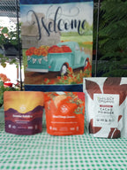 A collection of packaged food products arranged on a green-and-white checkered surface, including a decorative sign with a teal truck and flowers, a bag of Valdity Cacao Powder, an orange package, and a purple package.