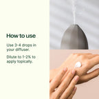 Hand applying a droplet of essential oil to wrist with diffuser in background